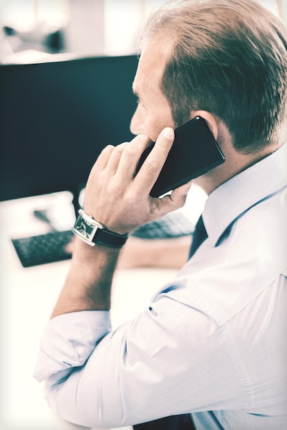 business, communication and technology concept- businessman with smartphone in office