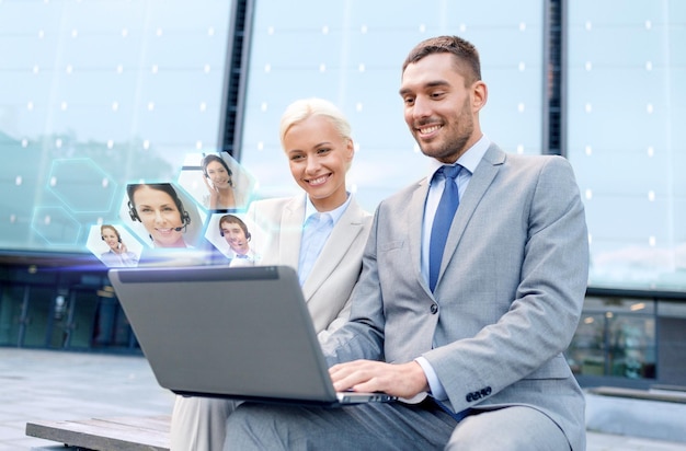 business, communication, technology and people concept - smiling businesspeople making video call or conference with laptop computer on city street