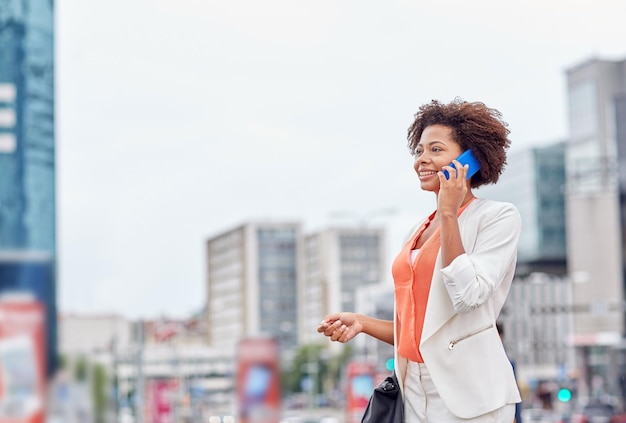 business, communication, technology and people concept - young smiling african american businesswoman calling on smartphone in city