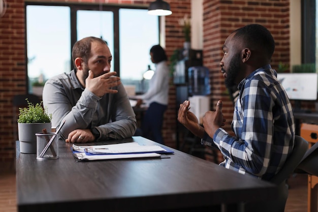 Reclutatore di giovani adulti di società commerciali che spiega la politica di lavoro del candidato di lavoro. direttore esecutivo che intervista un uomo sicuro di sé mentre esamina il cv e fa domande sull'esperienza lavorativa sul campo