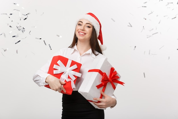 비즈니스 개념 색종이 축 하 벽과 선물 상자를 들고 산타 모자와 아름 다운 젊은 백인 비즈니스 우먼