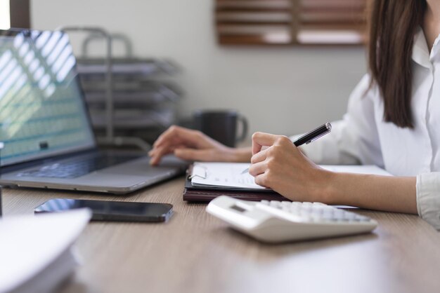 Business concept Businesswoman is reading business data on laptop and taking notes on document