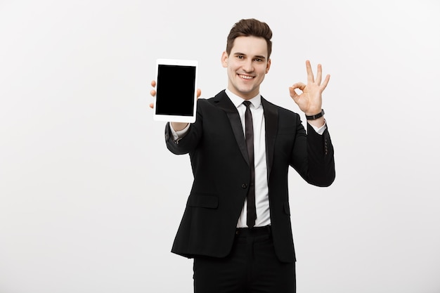 ビジネスコンセプト：大丈夫を示しているPCタブレットとスマートスーツの陽気なビジネスマン。灰色の背景の上に分離。