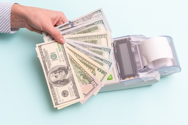 Business concept. Close-up of a female hand holding several hundred dollar bills above the cash register to pay for a product or service