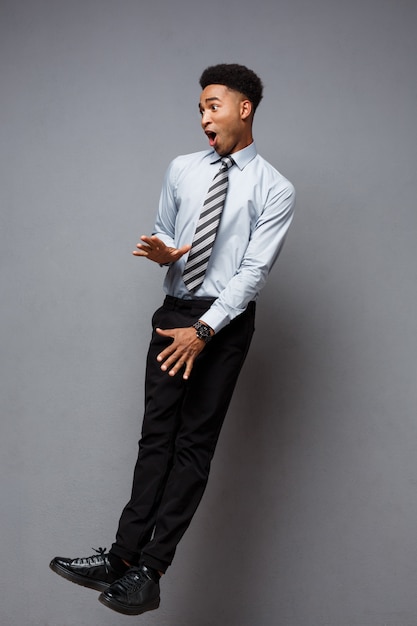 Business Concept - Full length portrait of successful african american businessman surprising jump in the office. 