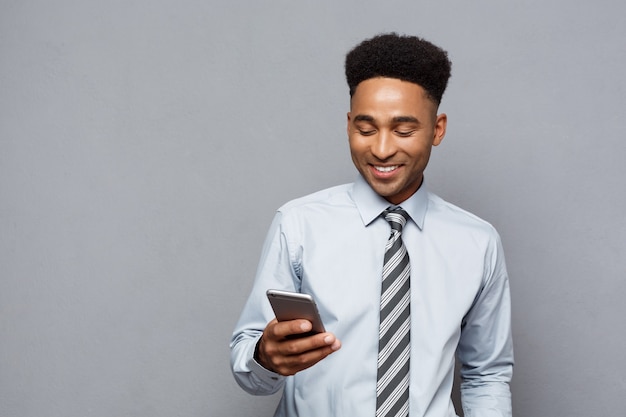 ビジネスコンセプト-携帯電話で幸せなハンサムなプロのアフリカ系アメリカ人ビジネスマンのテキストメッセージ。