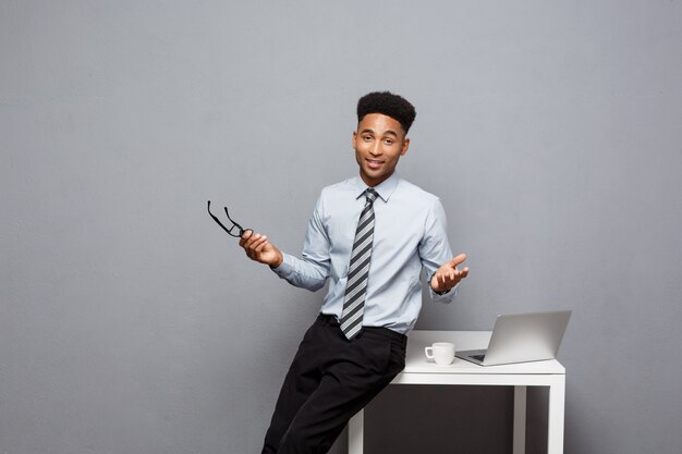 Business Concept - portrait of african american businessman with glasses having coffee sitting at a desk using a laptop. 