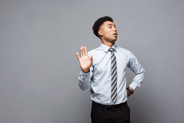 Business concept - portrait of stressed African American business man showing stop sign with hand on grey wall.