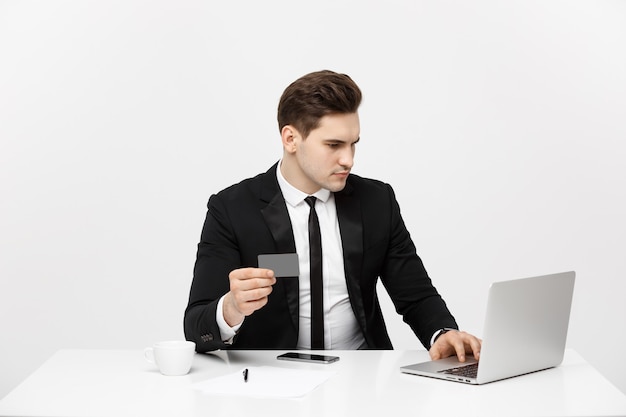 Business concept portrait of young businessman using laptop computer and mobile phone holding debit ...