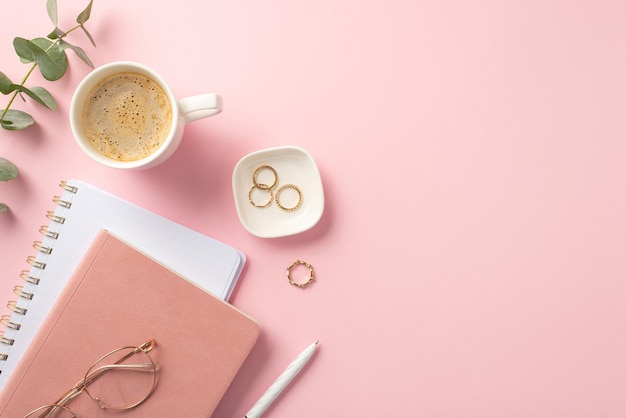 Photo business concept top view photo of workplace pink reminders pen glasses gold rings cup of coffee and eucalyptus on isolated pink background with copyspace