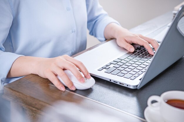 Business concept Woman in blue shirt typing on computer with coffee on office table backlighting sun glare effect close up side view copy space