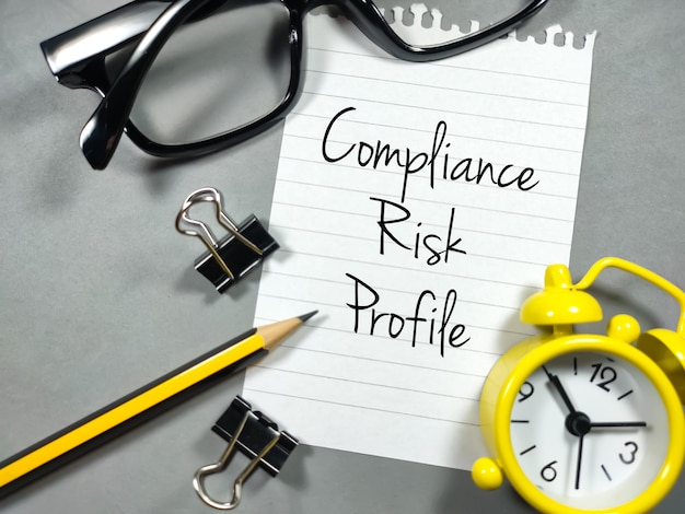 Фото Бизнес-концепция text compliance risk profile пишет на бумаге с скрепками, карандашом, очками и часами на сером фоне