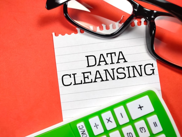 Бизнес-концепцияText DATA CLEANSING пишет на бумаге с очками и калькулятором на красном фоне