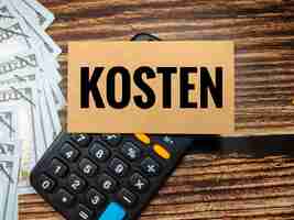 Photo business concepttext kosten with banknote and calculator on a brown wooden background