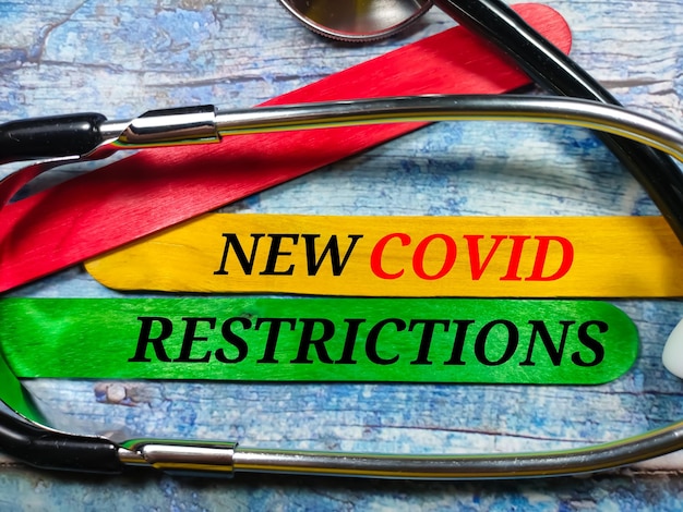 Business conceptText NEW COVID RESTRICTIONS with stethoscope and colored ice cream sticks on a wooden background