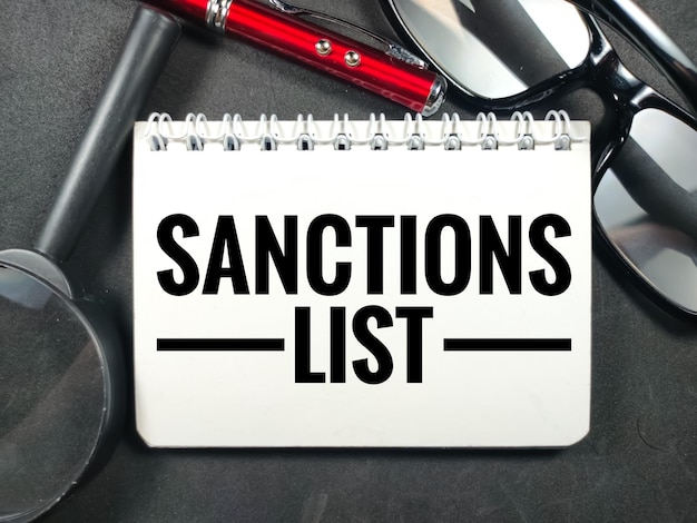 Business conceptText SANCTIONS LIST with penglasses and magnifying glass on black background