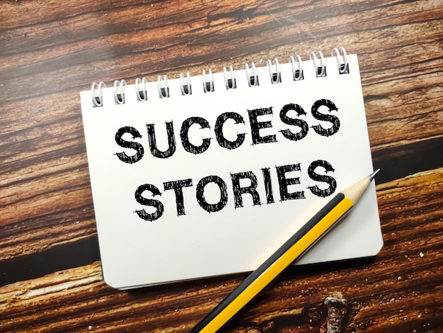 Business concepttext success stories on notebook with pencil on\
a wooden background