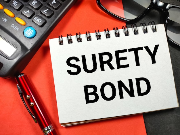 ビジネス コンセプトテキスト SURETY BOND ペン電卓とメガネ赤と黒の背景に