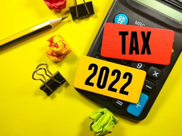 Business conceptText TAX 2022 on color board with torn paperpaper clipscalculator and pencil
