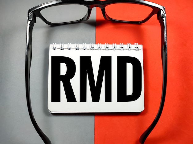 Business conceptWord RMD Required Minimun Distribution with glasses on gray and red background