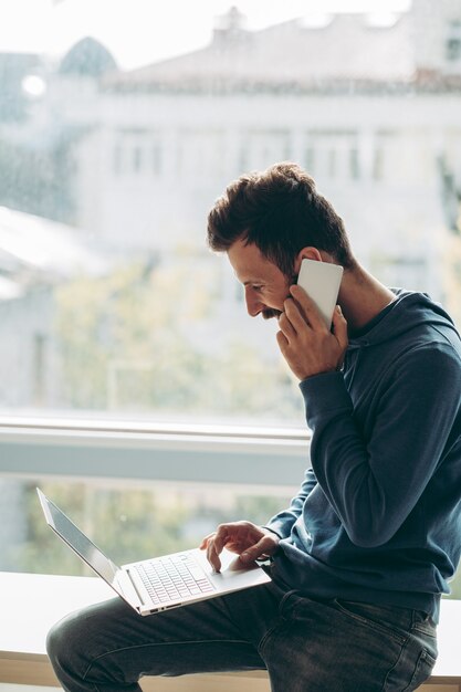 Business conversation on the mobile. Casual man sitting near the window and talking on the phone. Office work communication concept