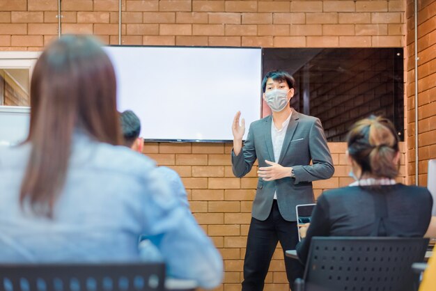 비즈니스 협력:젊은 아시아 남성 코치나 연사는 사무실 회의에서 다양한 사업가들에게 플립 차트 프레젠테이션을 합니다. 남성 교사 또는 트레이너는 다양한 동료에게 프로젝트를 제시합니다.