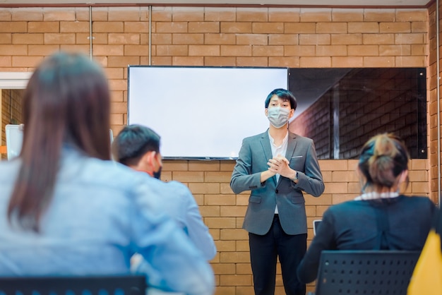 Business cooperation : young asian male coach or speaker make\
flip chart presentation to diverse businesspeople at meeting in\
office. male tutor or trainer present project to diverse\
colleagues.
