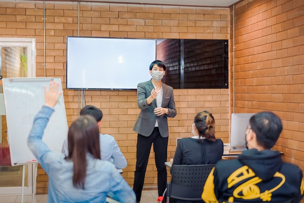 Business cooperation : Young asian male coach or speaker make flip chart presentation to diverse businesspeople at meeting in office. Male tutor or trainer present project to diverse colleagues.