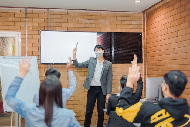 Business cooperation : Young asian male coach or speaker make flip chart presentation to diverse businesspeople at meeting in office. Male tutor or trainer present project to diverse colleagues.