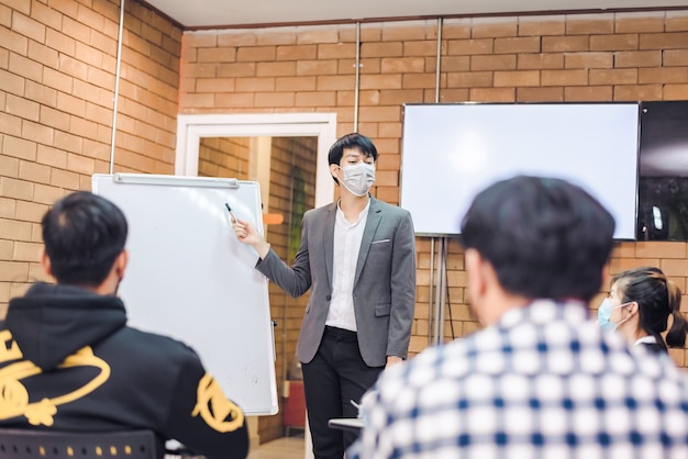 비즈니스 협력:젊은 아시아 남성 코치나 연사는 사무실 회의에서 다양한 사업가들에게 플립 차트 프레젠테이션을 합니다. 남성 교사 또는 트레이너는 다양한 동료에게 프로젝트를 제시합니다.