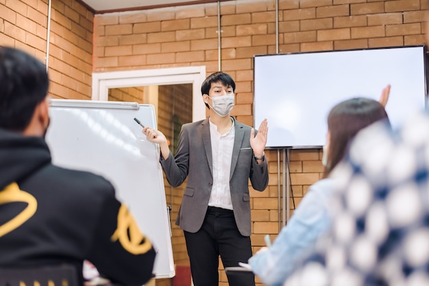 비즈니스 협력:젊은 아시아 남성 코치나 연사는 사무실 회의에서 다양한 사업가들에게 플립 차트 프레젠테이션을 합니다. 남성 교사 또는 트레이너는 다양한 동료에게 프로젝트를 제시합니다.