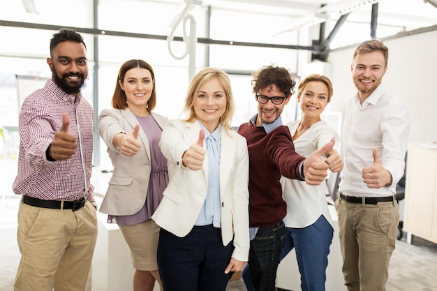 Foto concetto di business, corporate, persone, gesti e lavoro di squadra - felice team creativo sorridente che mostra i pollici in su in ufficio