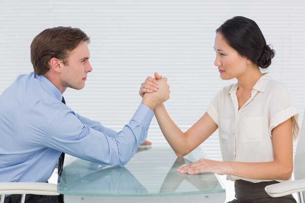 Business couple arm wrestling at desk