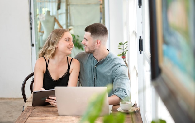 Business couple Cheerful woman using laptop in coffee shop Young businessman and happy girlfriend smiling while working together Two young businessmen sit together at the table