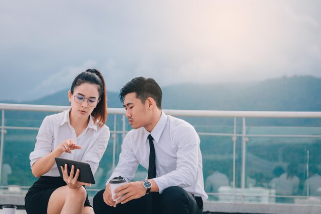 Photo business couple using mobile phone while sitting outdoors