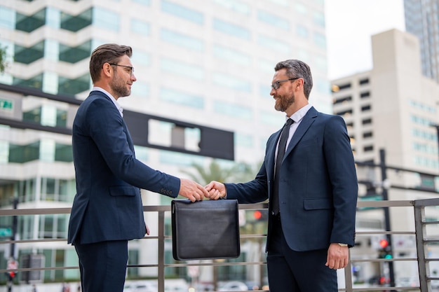 Business deal two business man hold business briefcase outdoor business transfer deal handover of a