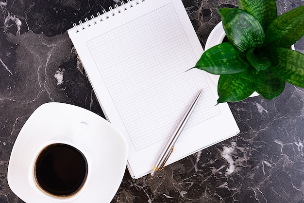 Business desk with notebook, pen, flower, on marble.