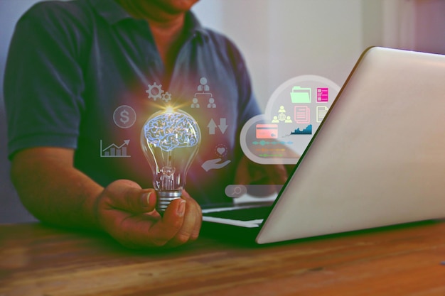 Бизнес-цифровая икона с мужчиной, держащим лампочку в руке во время работы с бизнес-концепцией ноутбука