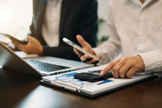 Business documents on office table with smart phone and calculator digital tablet and graph business with social network diagram and two colleagues discussing data working in the office