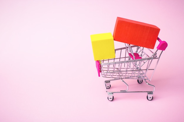 Business ecommerce concept Close up toy metal shopping cart with red yellow box inside on pink