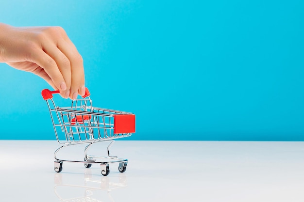 Business and ecommerce concept Closeup of hand using fingers pushing an empty mini shopping trolley while standing over a blue background in the studio Side view Space for text