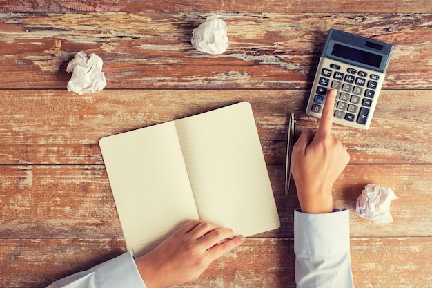 Photo business, education, people and technology concept - close up of female hands with calculator, pen and notebook on table