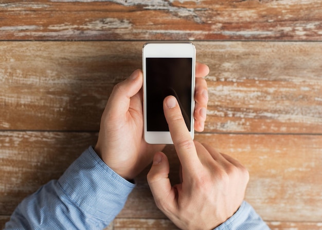 business, education, people and technology concept - close up of male hands holding smartphone and pointing finger to screen on table