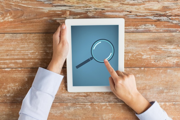 business, education, people and technology concept - close up of male hands with magnifying glass picture on tablet pc computer screen and coffee cup at table