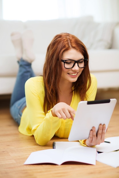 business, education and technology concept - smiling female student in eyeglasses with notebooks and tablet pc computer at home