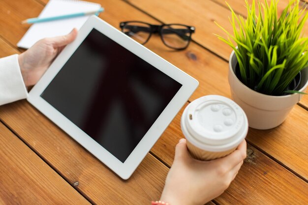 Foto concetto di business, istruzione, tecnologia, persone e pubblicità - primo piano della donna con lo schermo del computer pc tablet vuoto che beve caffè sul tavolo di legno