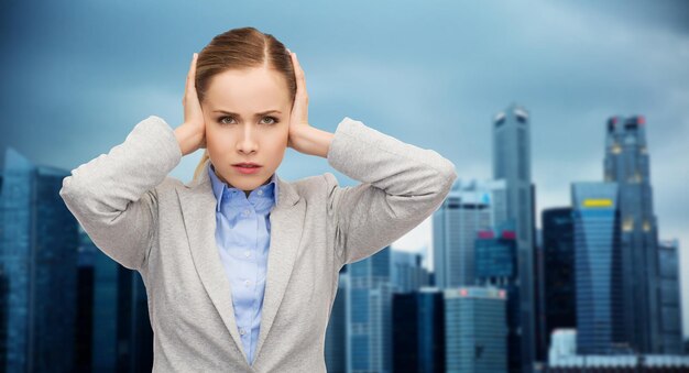 Foto concetto di affari, emozioni, stress, pressione e persone - donna d'affari stressata con orecchie coperte sullo sfondo della città