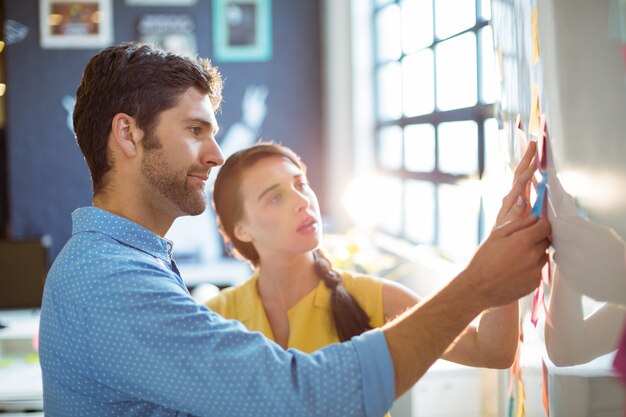 Business executive and co-worker putting sticky notes on whiteboard