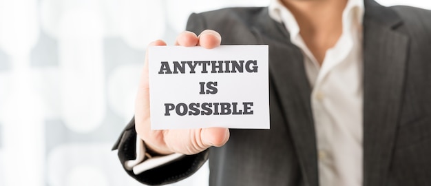 Business executive holding up a white card with Anything is possible sign in order to motivate his team