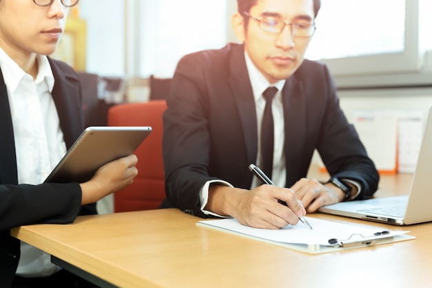 Business executive signing contracts with secretary at desk in office.